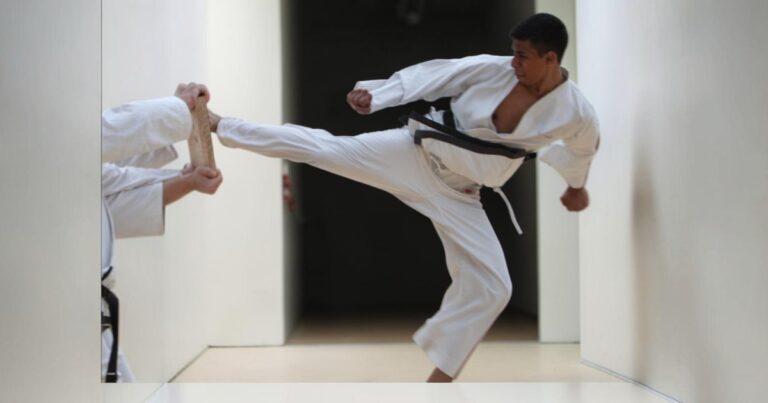 Male martial arts student wearing a white gi, demonstrating a board break
