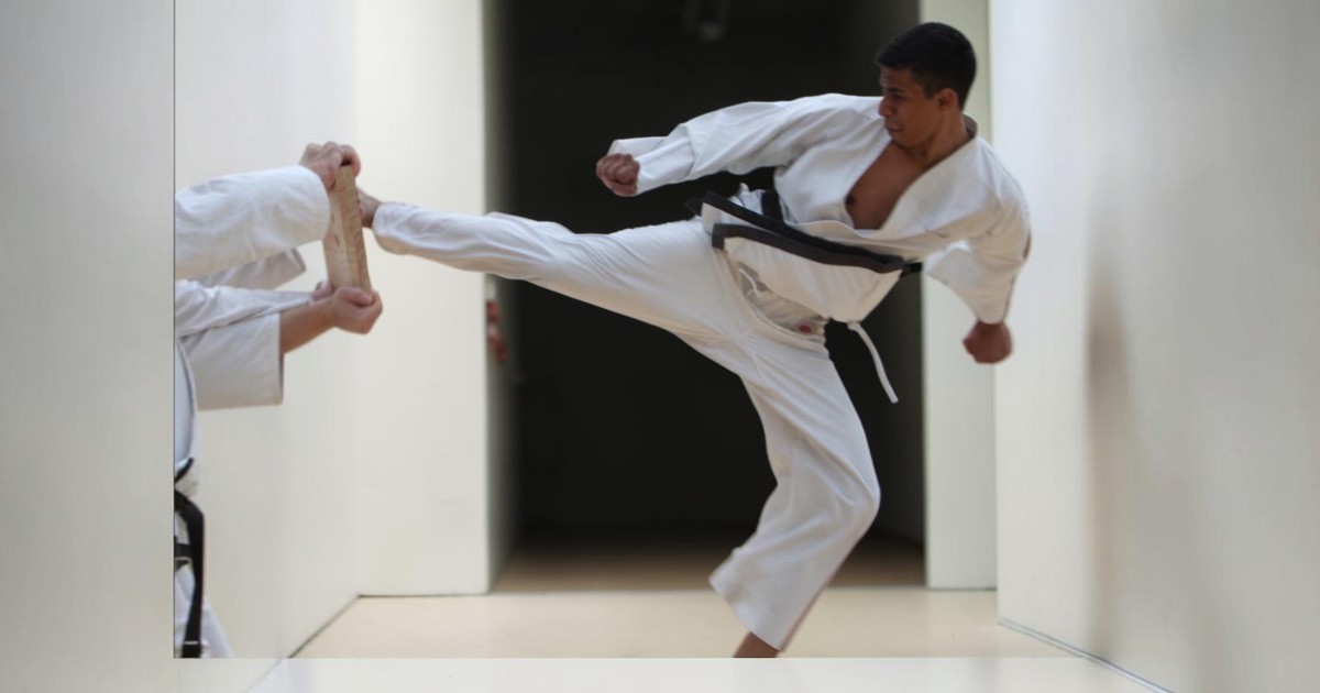 Male martial arts student wearing a white gi, demonstrating a board break